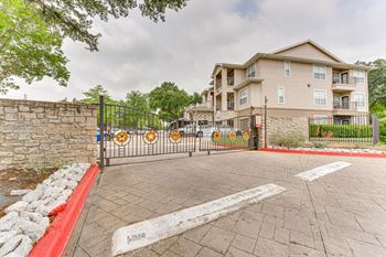 A gated entrance to a residential building with a stone wall and a red curb.